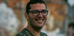 Homen sorridente usa óculos e encara a câmera