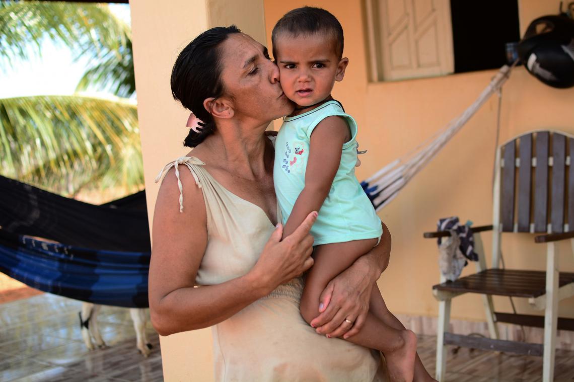 RosivÃ¢nia, uma mulher negra, segura seu filho bebÃª e o beija na bochecha. O menino olha em direÃ§Ã£o a cÃ¢mera.