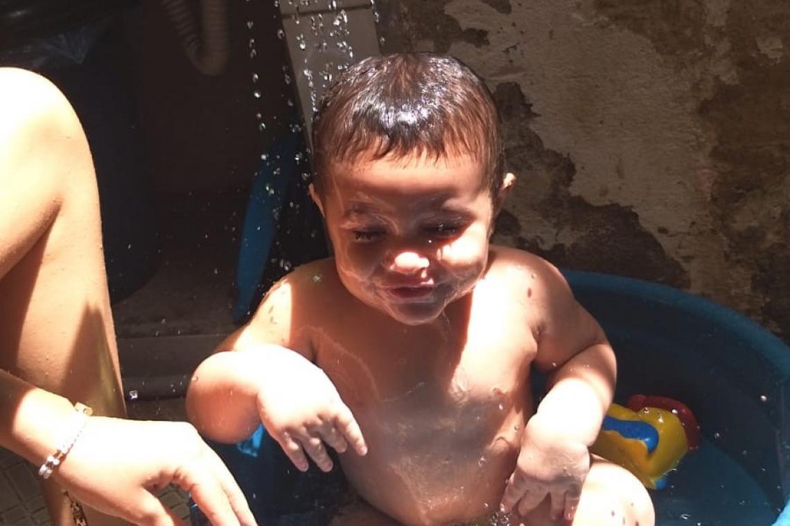 Um bebÃª aparece sorrindo enquanto toma banho em uma bacia