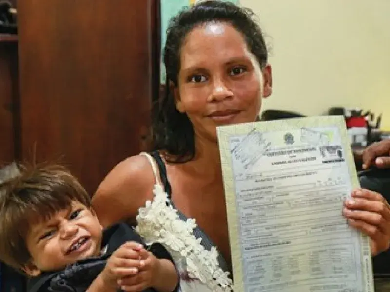 Mulher segura o filho e o registro de nascimento da criança nas mãos enquanto sorrir